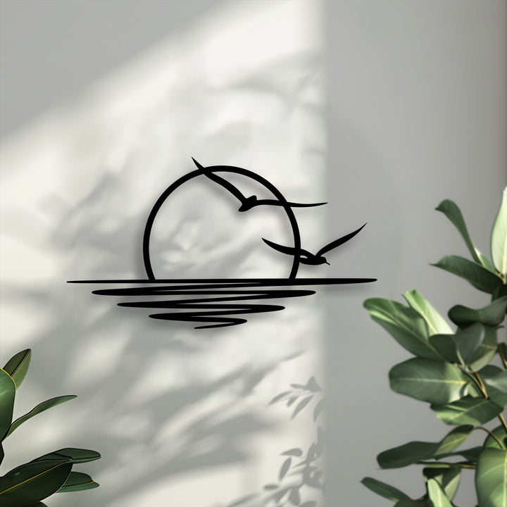 The striking black silhouette of a sunset with two soaring seagulls forms a prominent focal point as elegant metal art for wall.