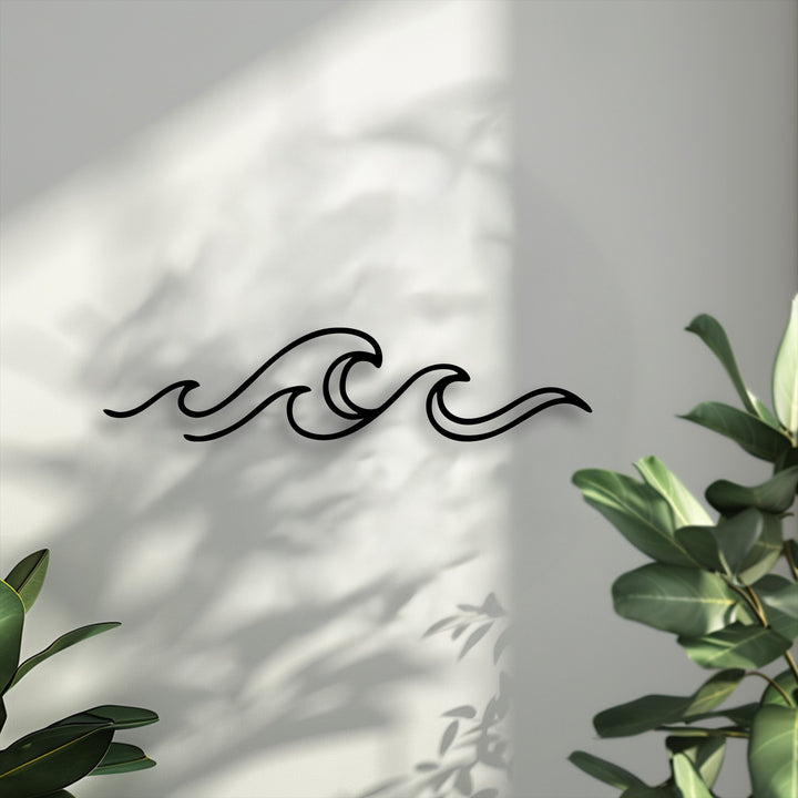 The focal point is a striking black minimal ocean wave metal artwork, elegantly displayed on a sunlit wall with soft plant shadows.
