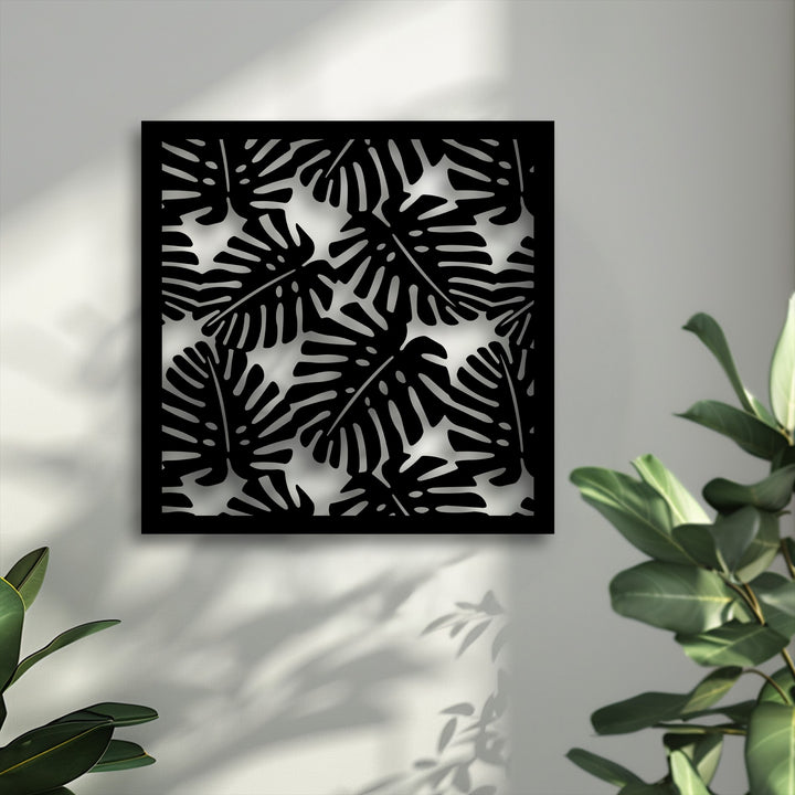 The geometric elements of this modern metal artwork showcase a striking black tropical monstera leaf pattern on a light wall, creating interesting shadows.