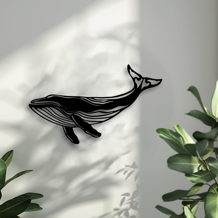 The cool, bright color temperature illuminates a stark black majestic whale silhouette metal wall decor, accented by soft green leaves.