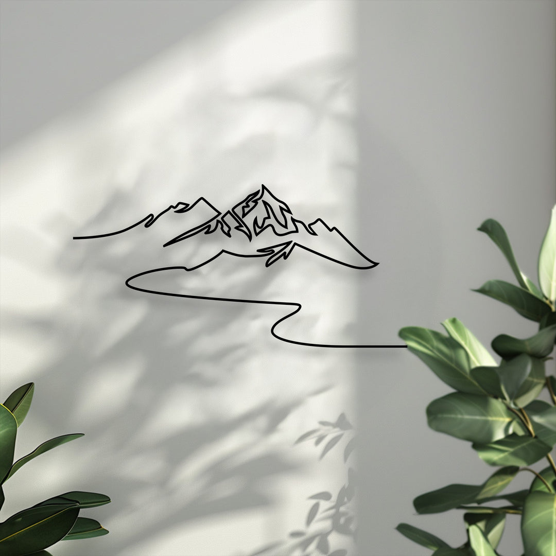The focal point is a striking black minimalist mountain line decorative metal art piece against a sunlit wall with leaf shadows.