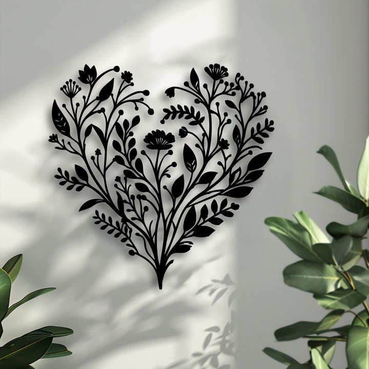 The intricate black botanical heart decoration wall art, silhouetted against a sunlit white wall, features a vibrant floral nature decor design.