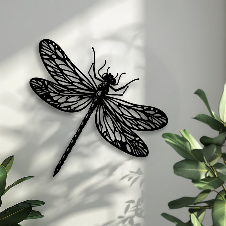 Highlighting depth and layers, the elegant metal dragonfly decoration wall art casts a shadow on a wall, accented by green foliage.