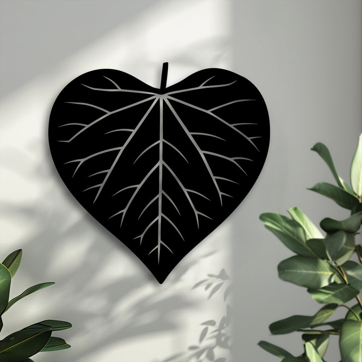 The visual rhythm of dappled light and dark shadows beautifully enhances the elegant heart-shaped leaf silhouette, a unique metal wall art piece.