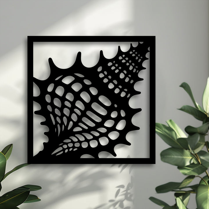A vertically oriented square black-framed unique metal wall art piece features an intricate, organic seashell-like shape.