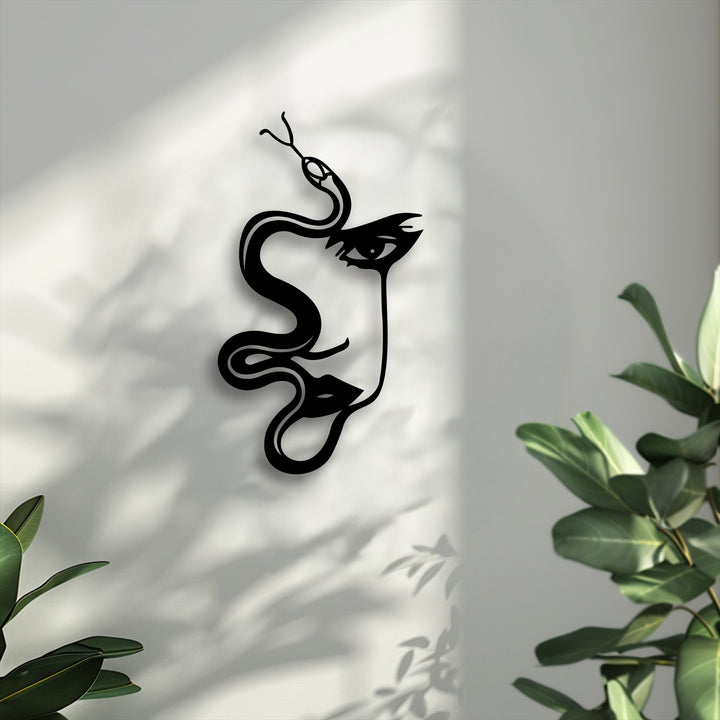 The decorative metal art, an intricate abstract woman and serpent silhouette, is the focal point on a textured white wall with plant shadows.