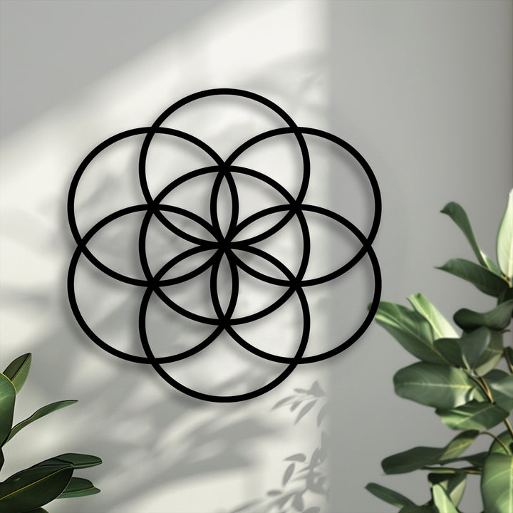 The prominent focal point is the black Sacred Balance Flower of Life metal wall decor, intricately designed against a softly lit wall with shadows.