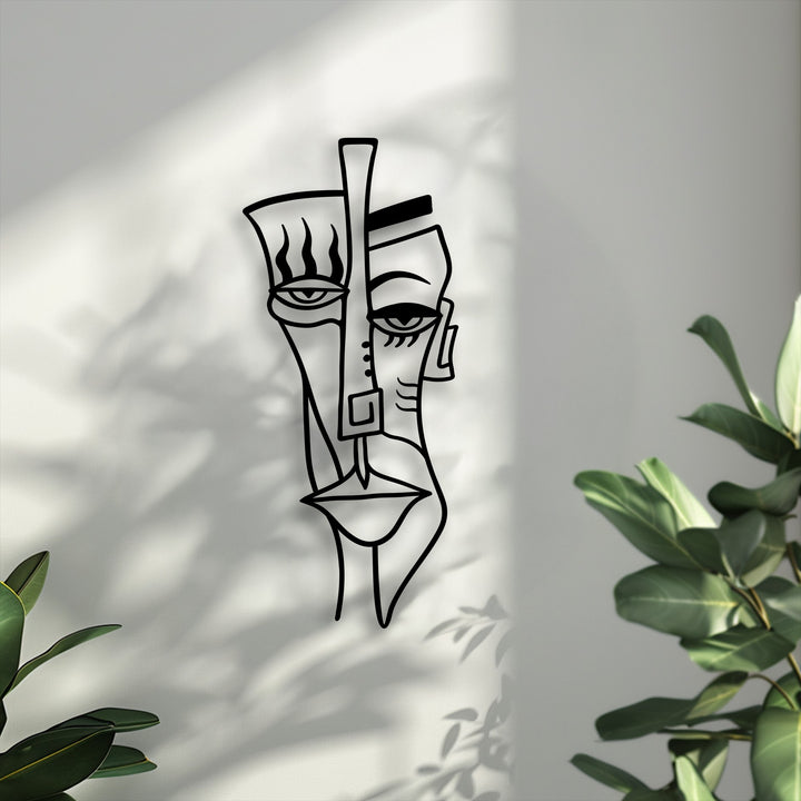 Soft, diffused shadows from leafy plants gently fall upon the textured wall, showcasing the striking abstract face decorative metal art.