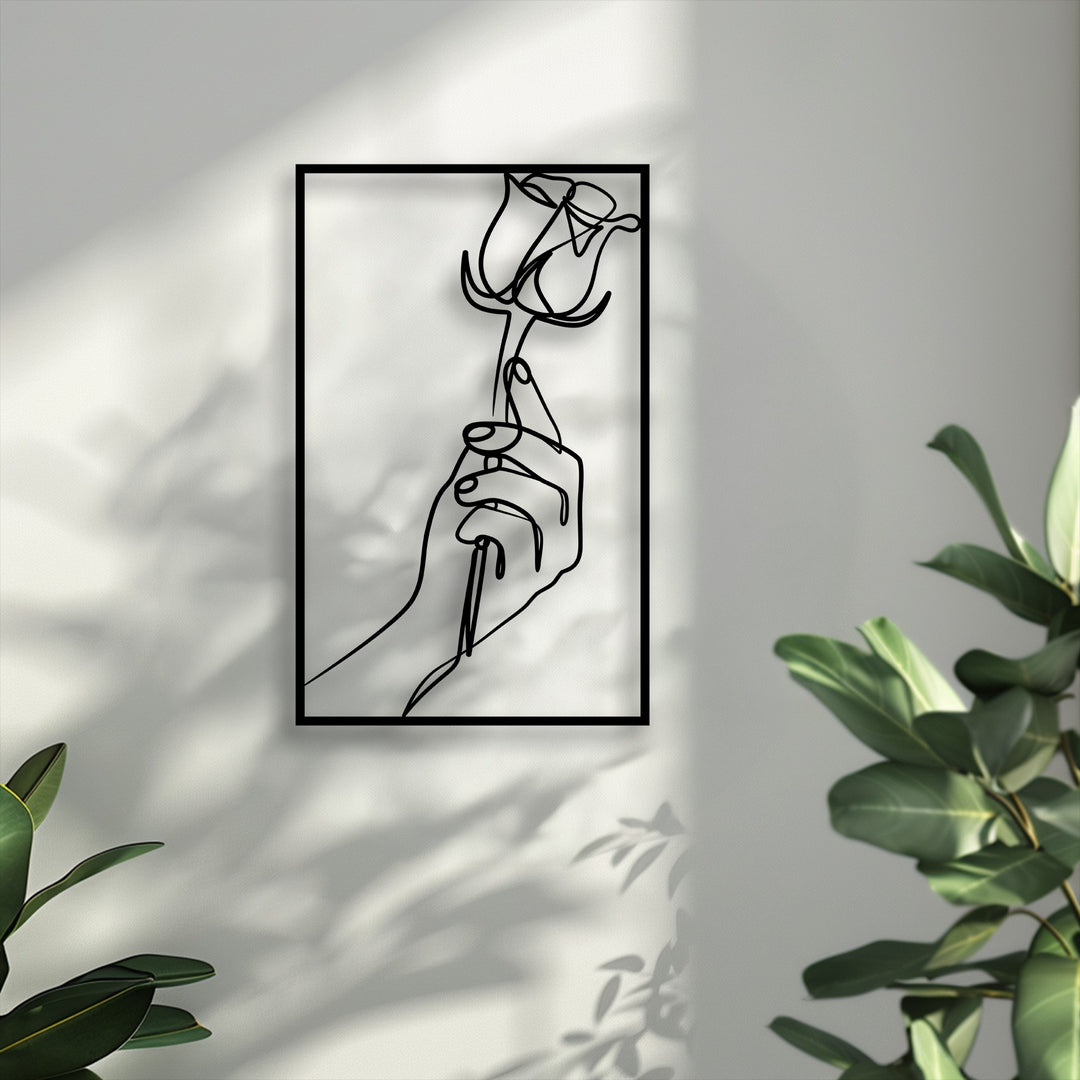 Subtly desaturated tones emphasize the elegant unique metal wall art featuring a minimalist hand holding a rose, surrounded by natural light.