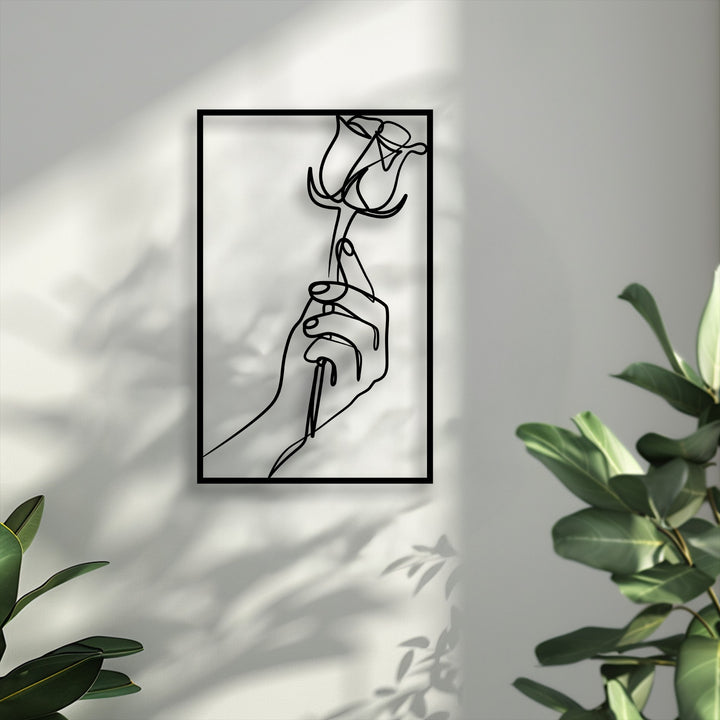 Subtly desaturated tones emphasize the elegant unique metal wall art featuring a minimalist hand holding a rose, surrounded by natural light.