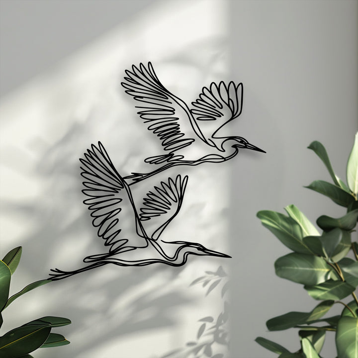 The focal point features two graceful flying herons, crafted as unique metal wall art, casting elegant shadows on a textured wall.