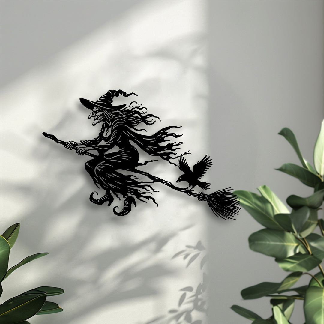Featuring impressive depth and layers, this Flying Witch metal art for wall casts sharp shadows on the light wall, interacting with leafy green plants.