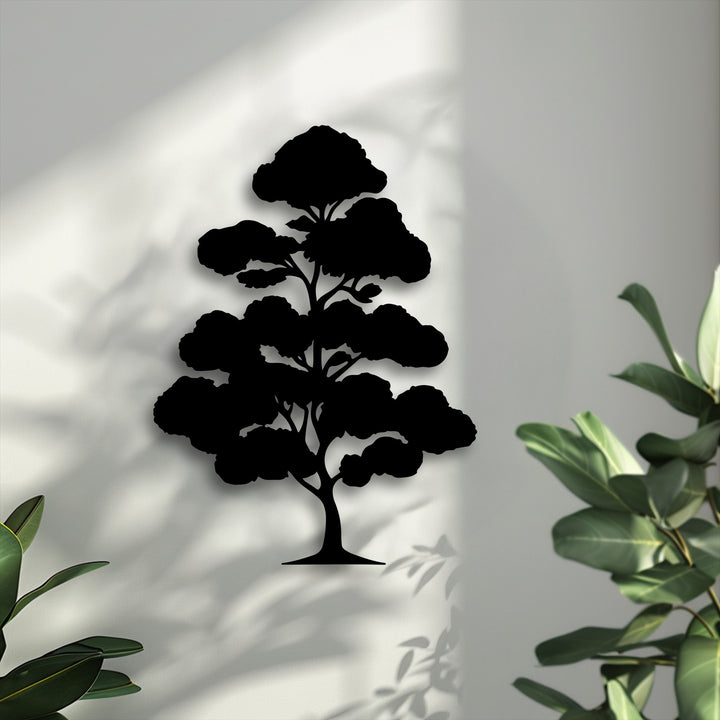 A serene black silhouette of a bonsai tree, a unique metal wall art piece, is centered on a textured light wall with soft background shadows.