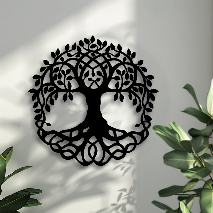 The intricate negative space of the black Celtic Tree of Life metal artwork highlights the white wall's texture, complemented by soft plant shadows.