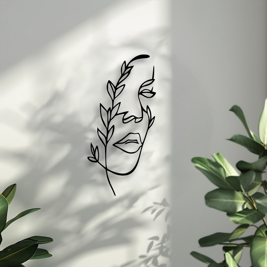 Dramatic shadows of leaves and light streaks fall across a white wall, highlighting the elegant black decorative metal art of a minimalist female line face.