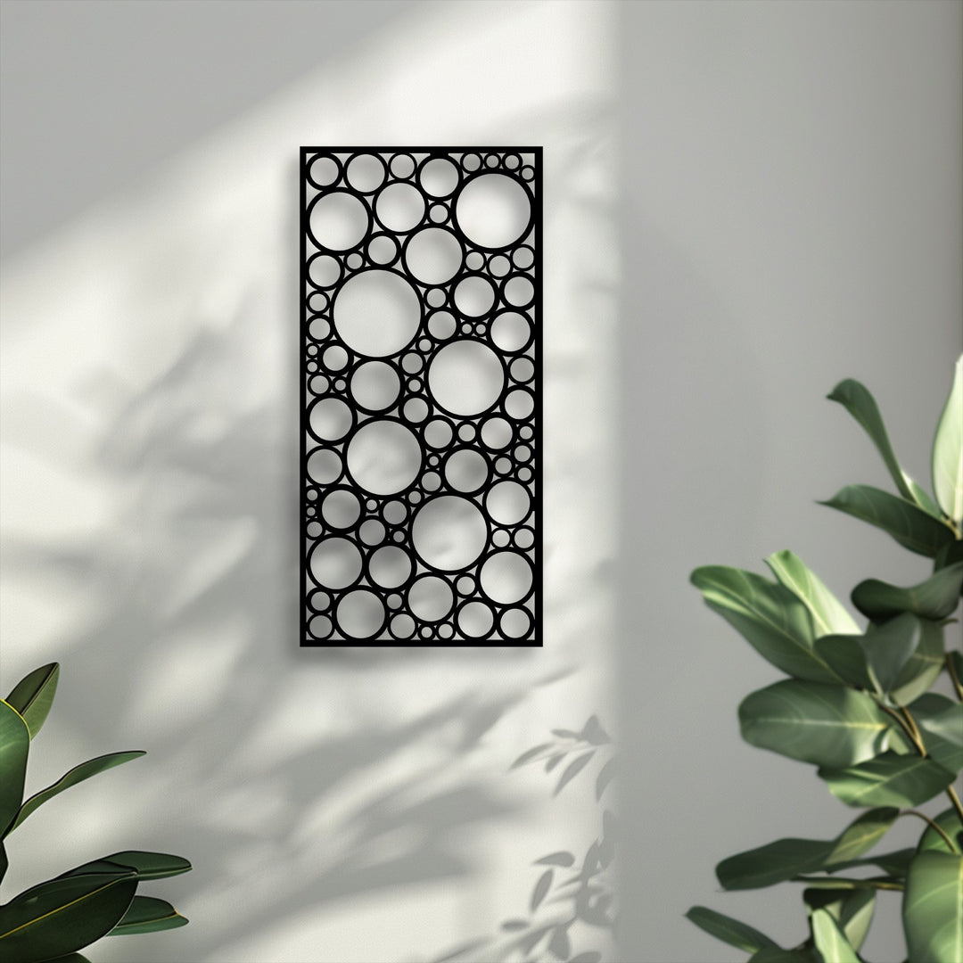 A pristine light gray wall showcases a black geometric circle pattern panel, a modern decoration wall art piece, with soft plant shadows.