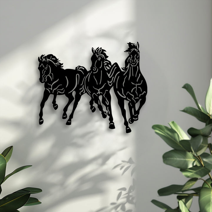 The color saturation highlights the bold black galloping trio horses metal decoration wall art against a muted background with green plants.