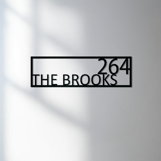 The realistic detail shows the precision-cut modern metal artwork of the personalized family name sign, a minimalist address plaque with a visible drop shadow on the wall.