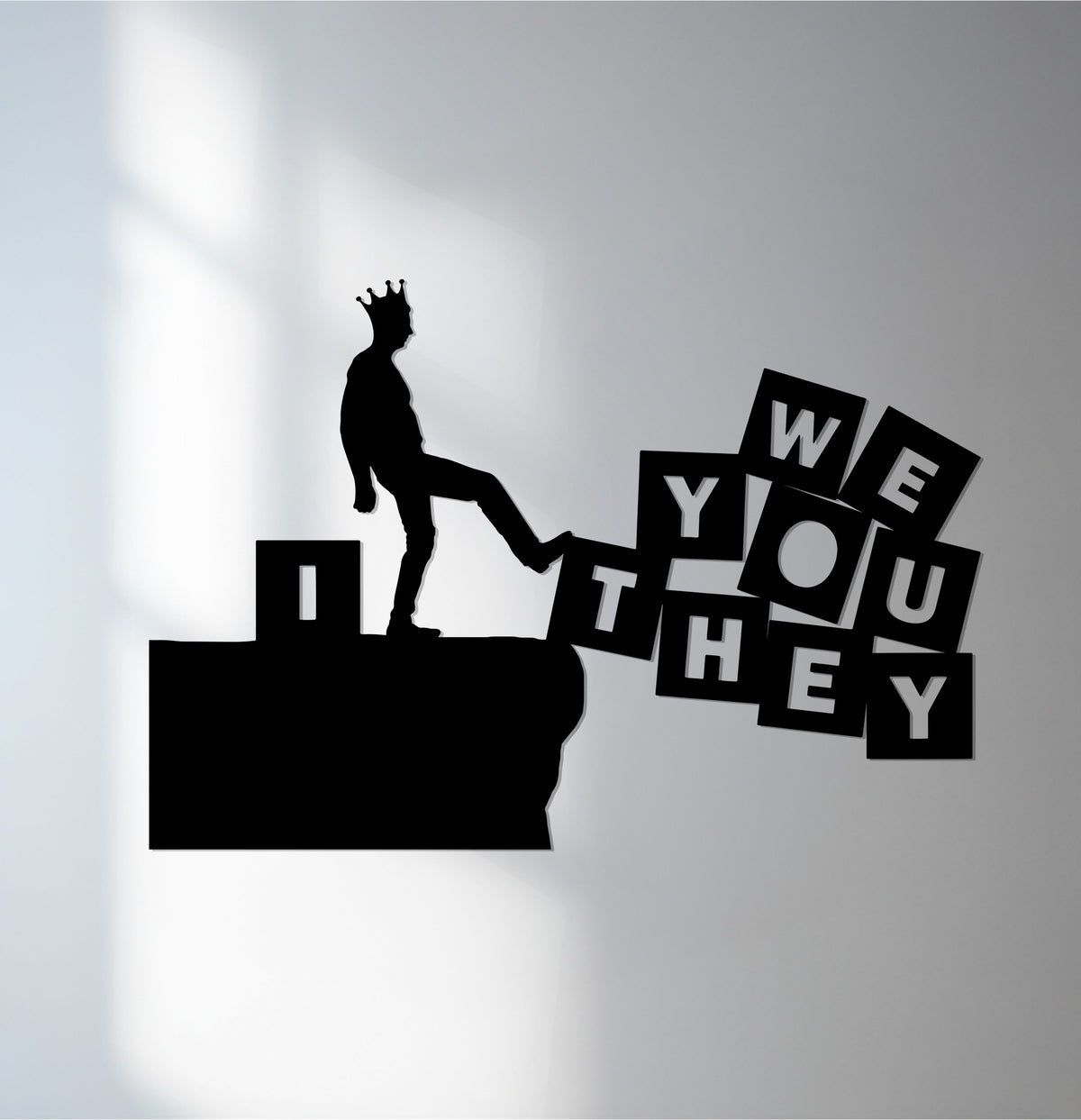 A regal silhouette balances precariously, stepping on layered 'WE,' 'YOU,' and 'THEY' blocks, creating a dynamic metal artwork with striking depth.