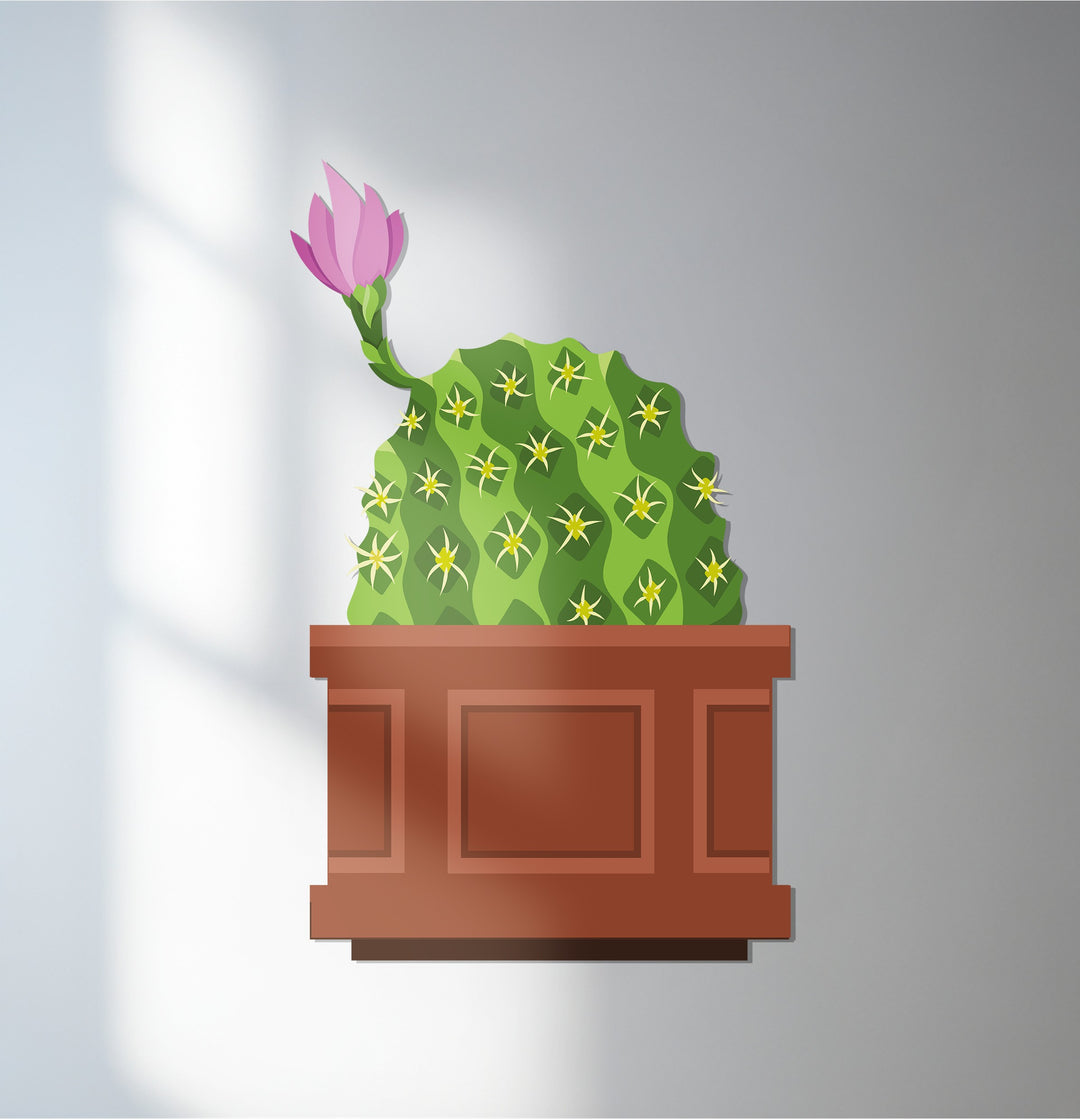 The decorative metal art features a rectangular planter filled with a geometric cactus and a blooming pink flower, creating a modern botanical design.
