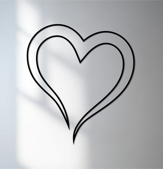 Neutral color temperature highlights the black double line heart, a piece of unique metal wall art, against the subtle gradations of the wall's surface.