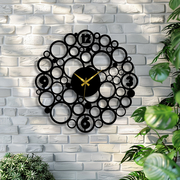 The black finish of the decorative metal art clock highlights its bubble circle design, creating a bold contrast against the white brick wall.