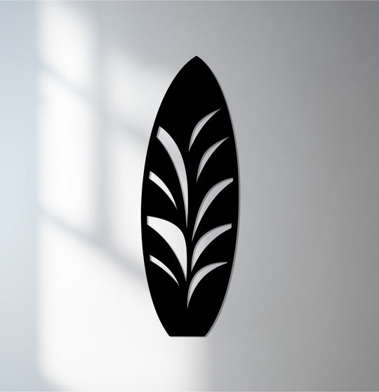 The focal point of this black surfboard is the metal artwork depicting a tropical leaf design, offering modern coastal decor.