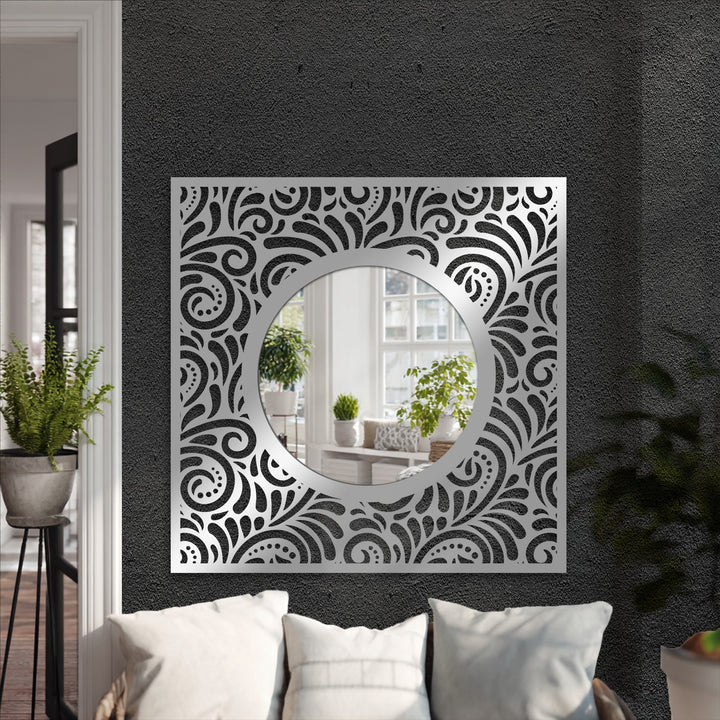Reflecting a bright room, the ornate eclipse framed wall mirror showcases a black metal patterned square frame with a round center.