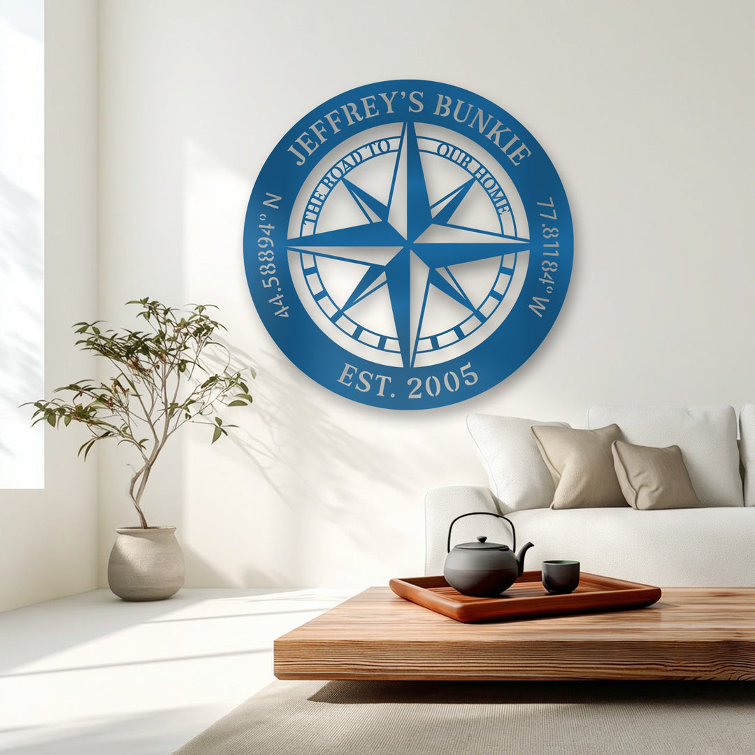 The vibrant blue personalized compass metal artwork strongly contrasts with the crisp white wall, accentuating its custom name.