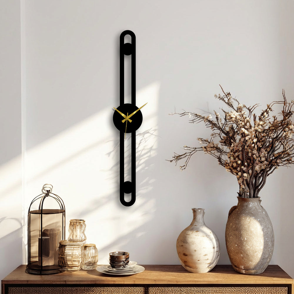 A white wall provides a clean backdrop, highlighting the minimalist vertical metal wall clock and complementing the decorative metal art on the surface below.