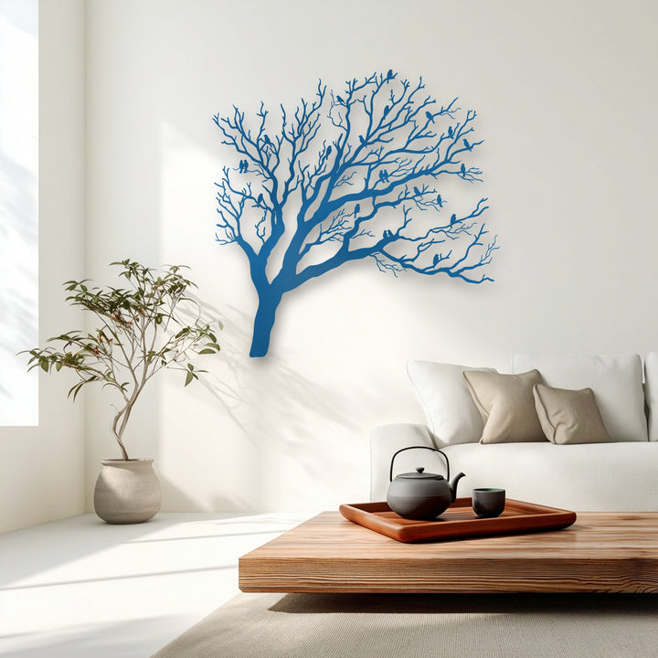 The striking color contrast of the vibrant blue unique metal wall art depicting birds on bare tree branches stands out against the white wall.