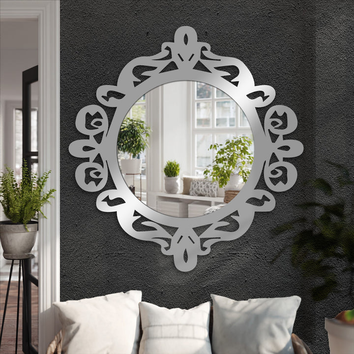 Ornate royal crest round bathroom mirror with a decorative design in silver, reflecting a sunlit room with plants and complementing the dark textured wall behind.