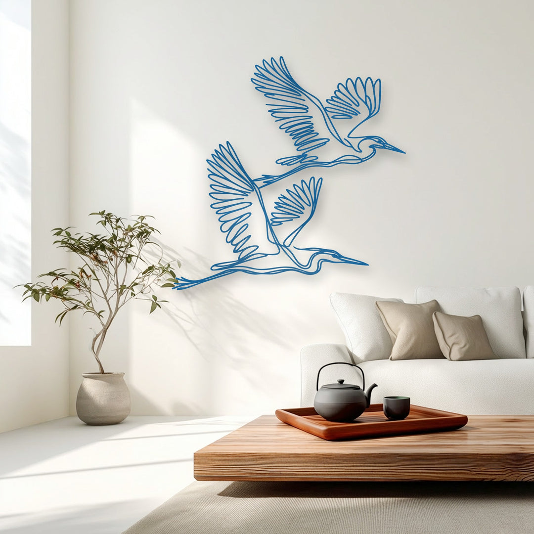 Vibrant blue minimalist flying herons, a stunning metal art for wall, emerge as the focal point on the clean white wall.