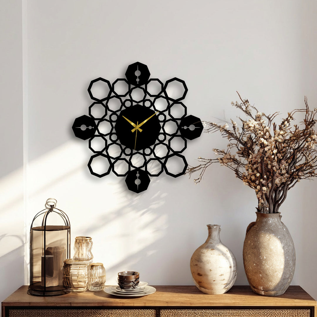 A striking black geometric mandala clock, a prime example of decorative metal art, prominently features golden hands against a clean white wall.