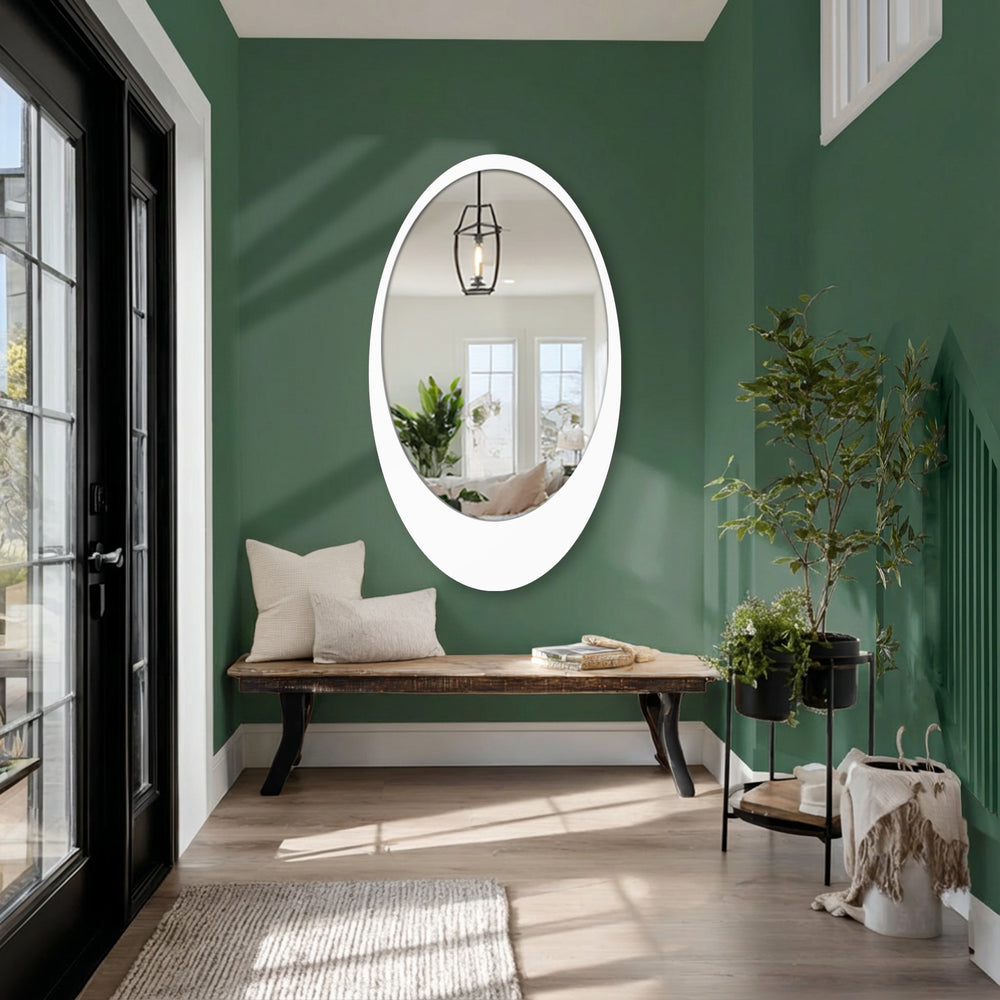 Illuminating the scene, the brightest area in the sleek minimal oval floor mirror reveals an interior, reflecting a modern mirror design in a hallway setting.