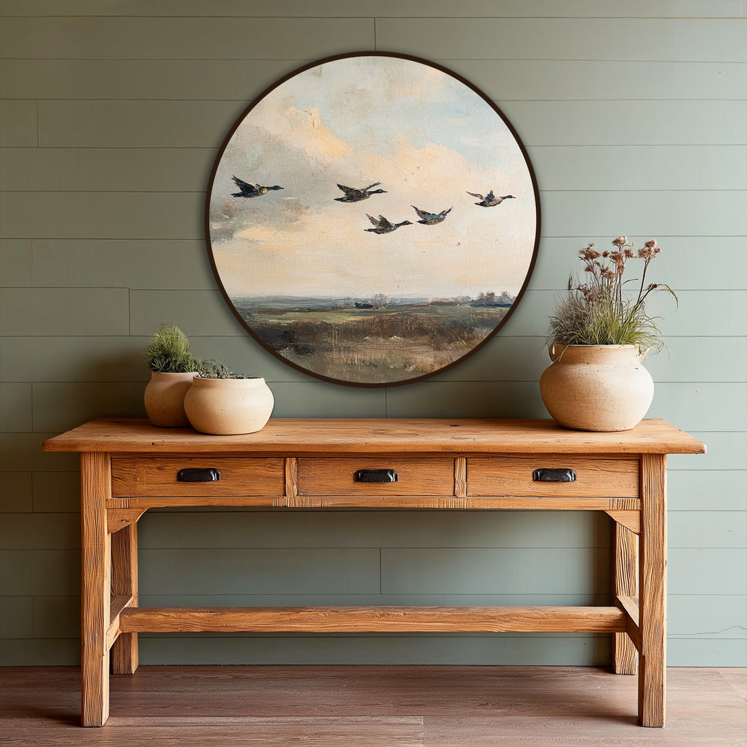 Visual rhythm in the quiet migration oil painting decoration is achieved through the repeated shapes of ducks in flight across the circular vintage landscape.