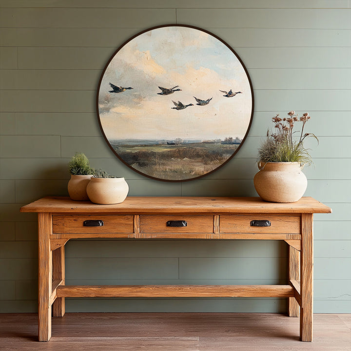 Visual rhythm in the quiet migration oil painting decoration is achieved through the repeated shapes of ducks in flight across the circular vintage landscape.