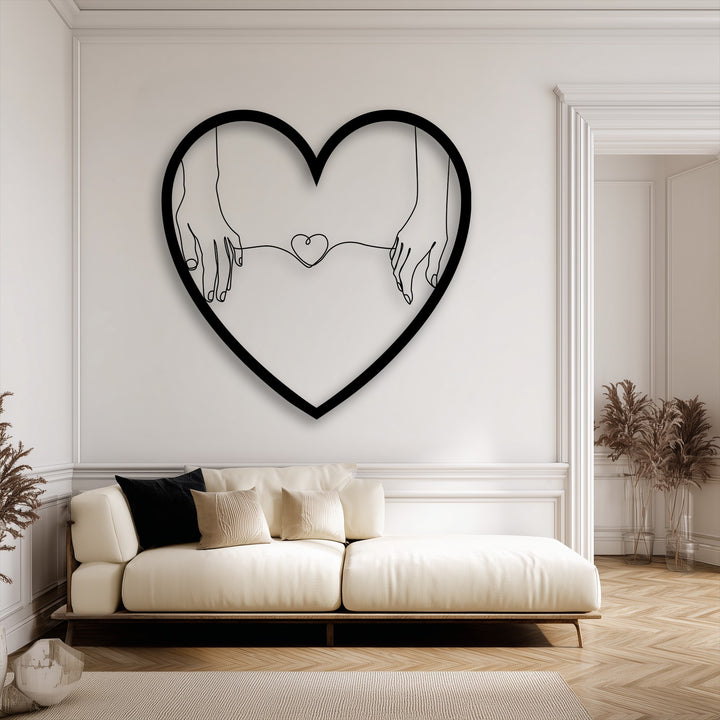 The dimensional layering effect of the minimalist heart-shaped metal wall decor highlights hands holding a connected heart within its silhouette.