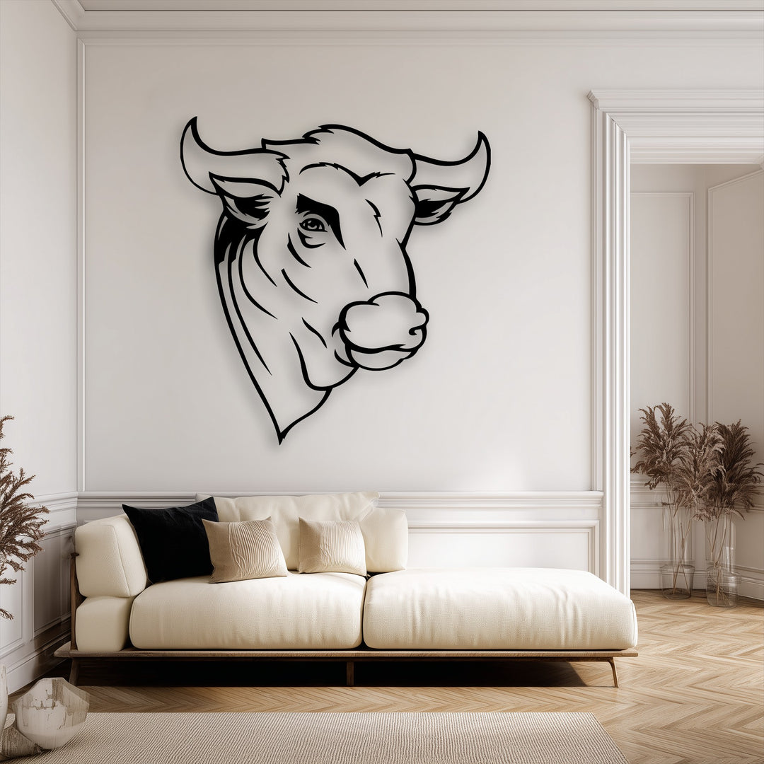 With low color saturation, this image highlights a striking black rustic bull head decorative metal art piece against a soft cream wall in a minimalist interior.