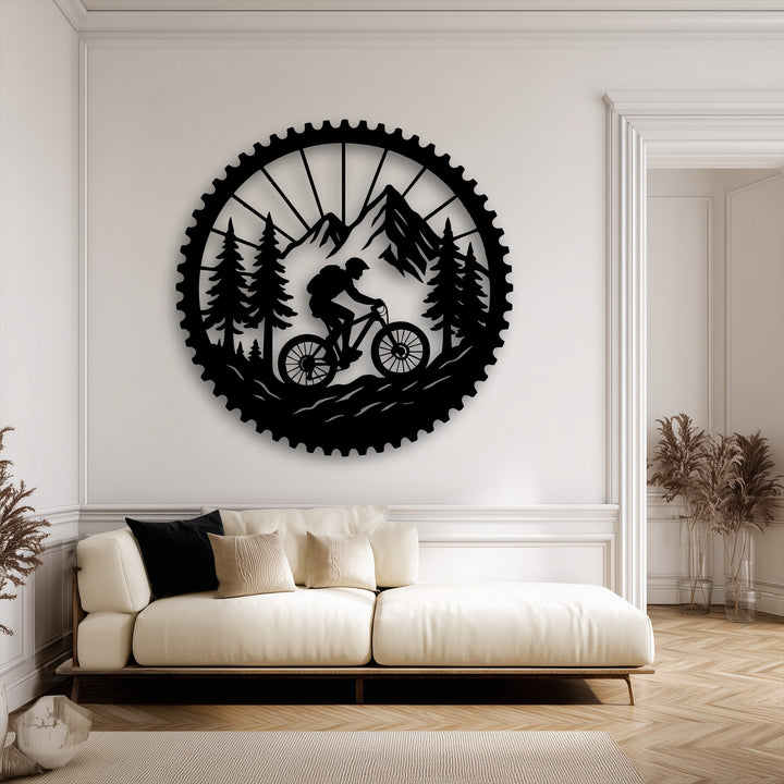 The negative space in this detailed metal artwork creates a stark silhouette of a mountain biker, forest, and mountains within a large gear.