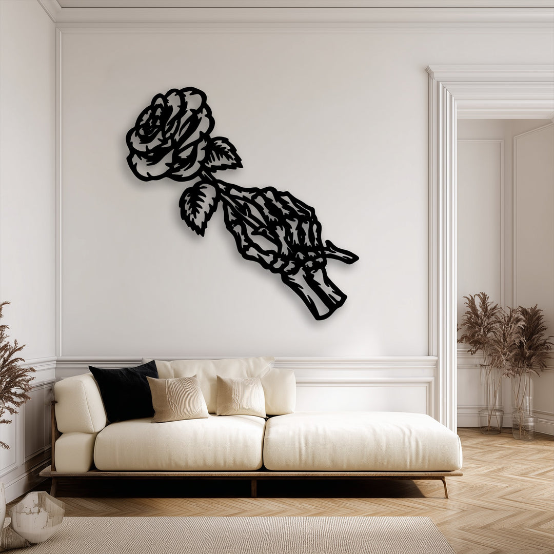 The realistic detail of this decorative metal art showcases a black skeleton hand delicately holding a fading gothic rose on a white wall.