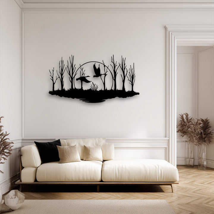 The abstract form of this decorative metal art captures a minimalist forest silhouette with graceful flying birds against a circular moon.