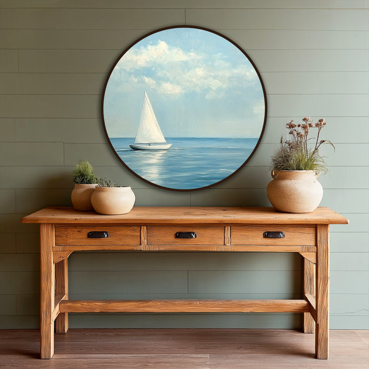A serene oil painting artwork showcases a minimalist sailboat in a round frame, evoking a calm and peaceful mood with its soft blues and reflective light.