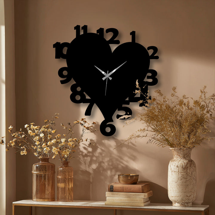 The muted color saturation of this scene highlights a black heart shape number metal artwork wall clock, contrasted with warm, desaturated dried flowers.
