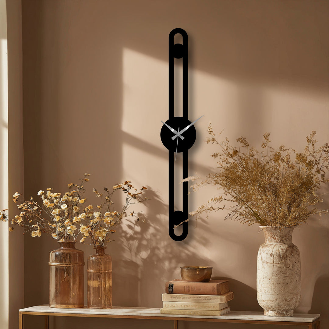 The vertical metal wall clock creates visual rhythm with its slim linear design, adding a modern element to home decor.