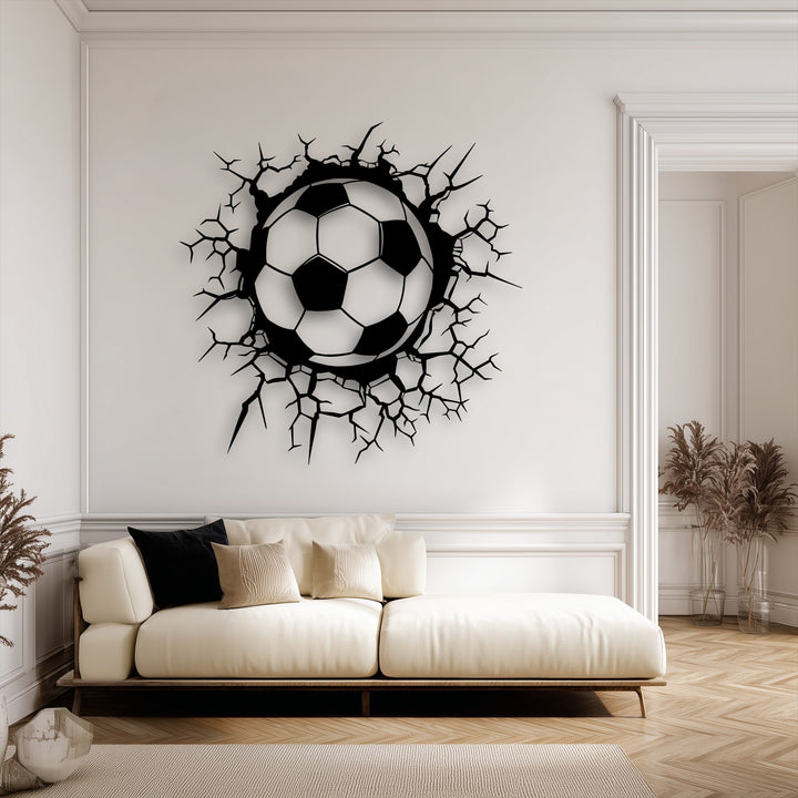 Warm ambient lighting highlights this breaking wall soccer ball metal wall art, an engaging decoration wall art piece above a neutral-toned sofa.