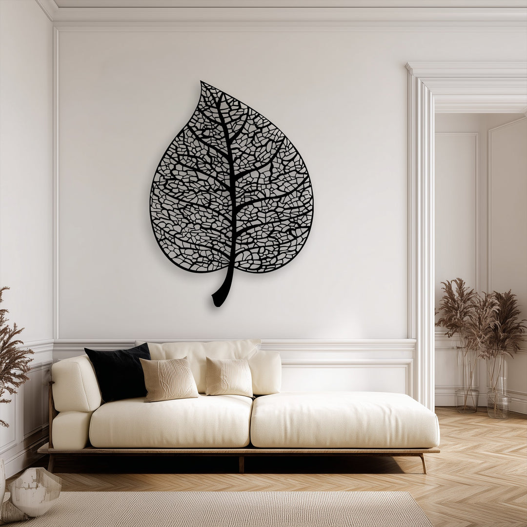 The sharp transition from the deep black decorative metal art to the warm, creamy wall enhances the intricate botanical leaf.