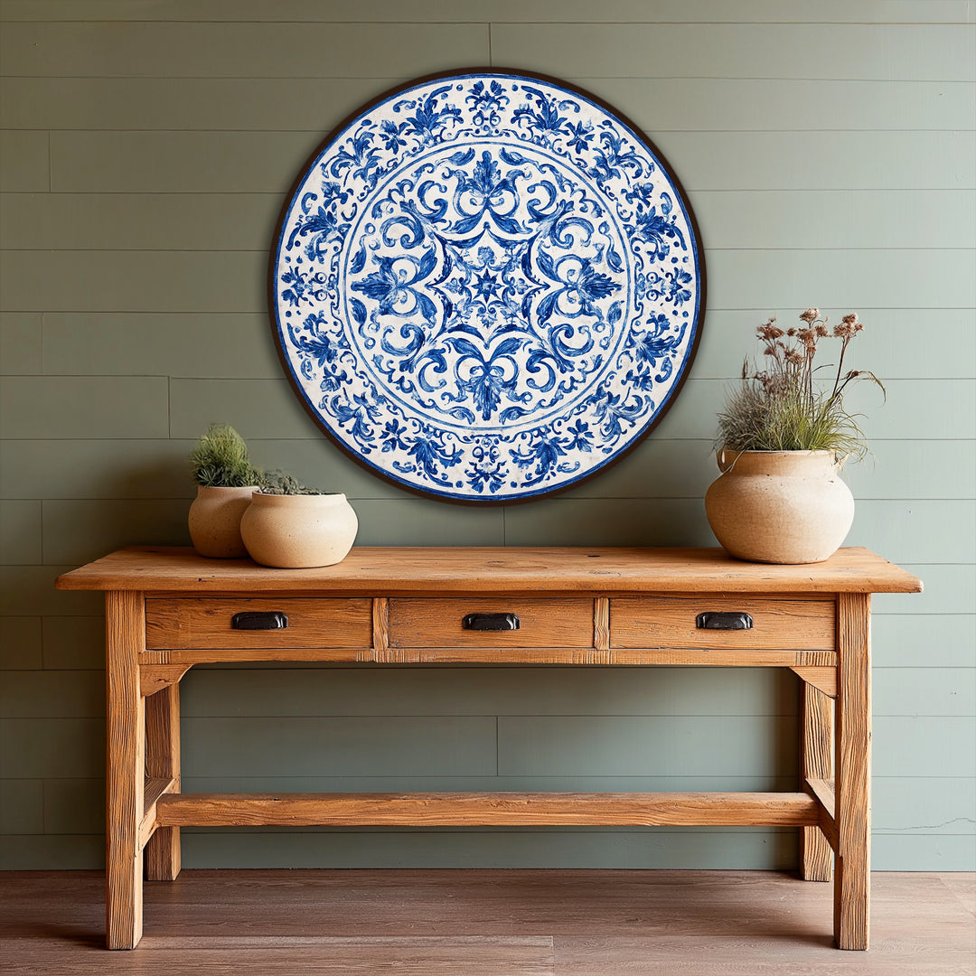 Negative space highlights the patterned center of this round oil painting home decor, revealing a classic blue ornamental design on an easel-style wooden table.