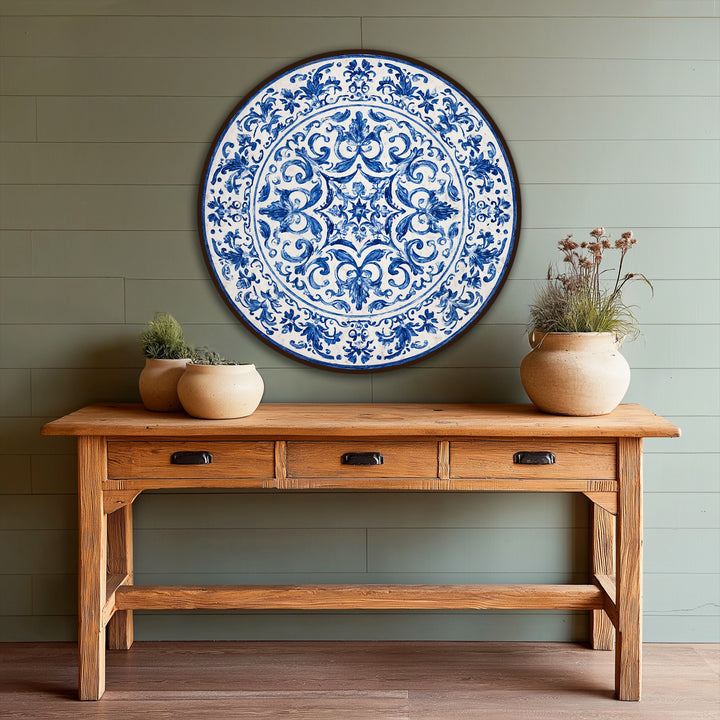 Negative space highlights the patterned center of this round oil painting home decor, revealing a classic blue ornamental design on an easel-style wooden table.