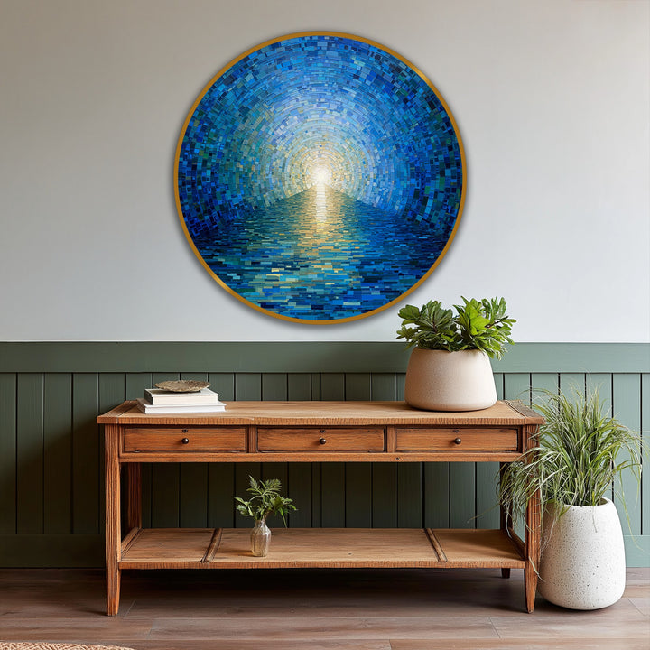 Foreground focus on a wooden console table displaying a radiant horizon round oil painting art piece of a blue mosaic ocean with a golden frame.